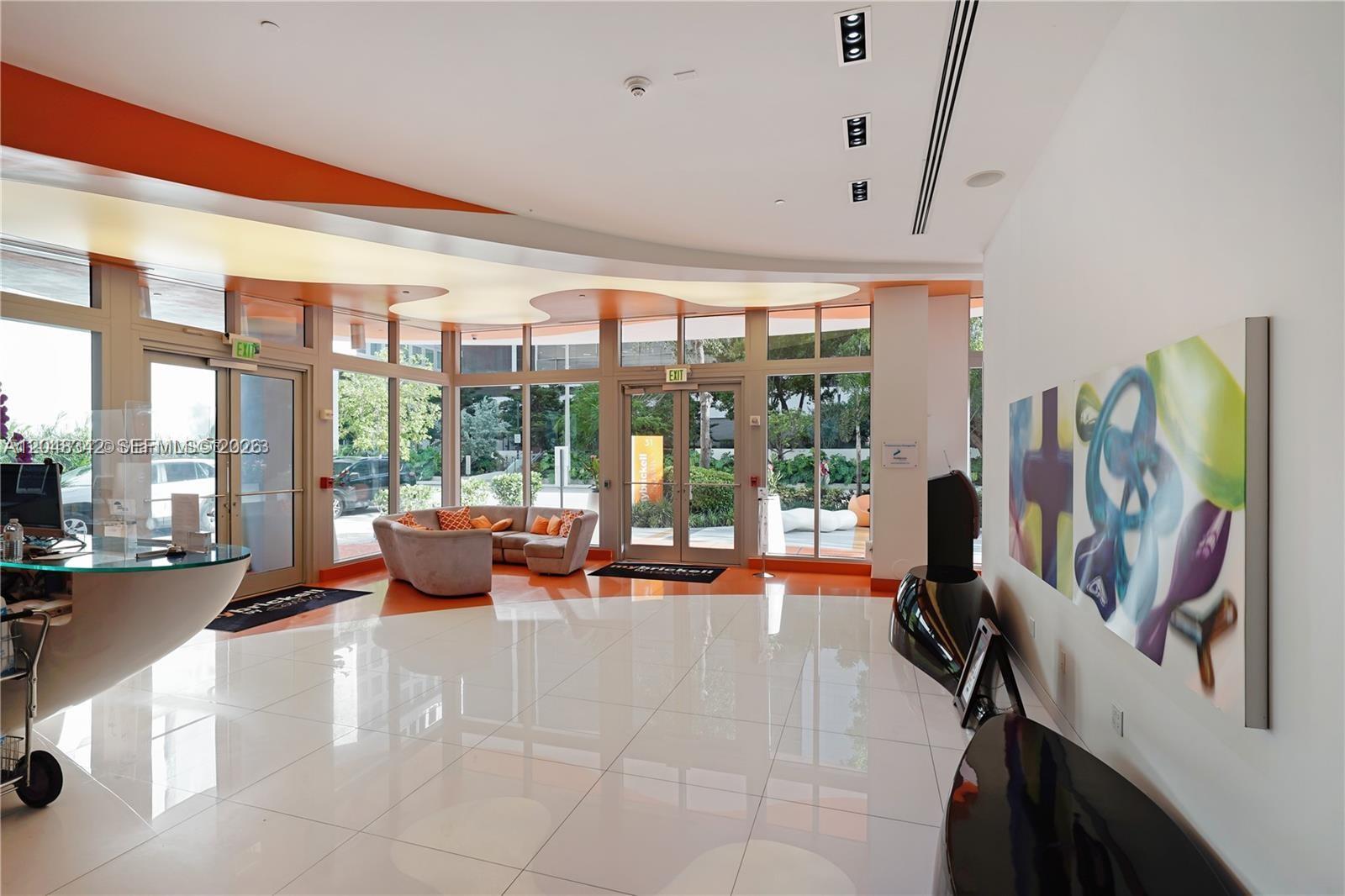 A modern lobby features white tile floors, a curved reception desk, and floor-to-ceiling windows — 31 SE 6th St # 2706, Miami FL 33131, MIAMI, FL