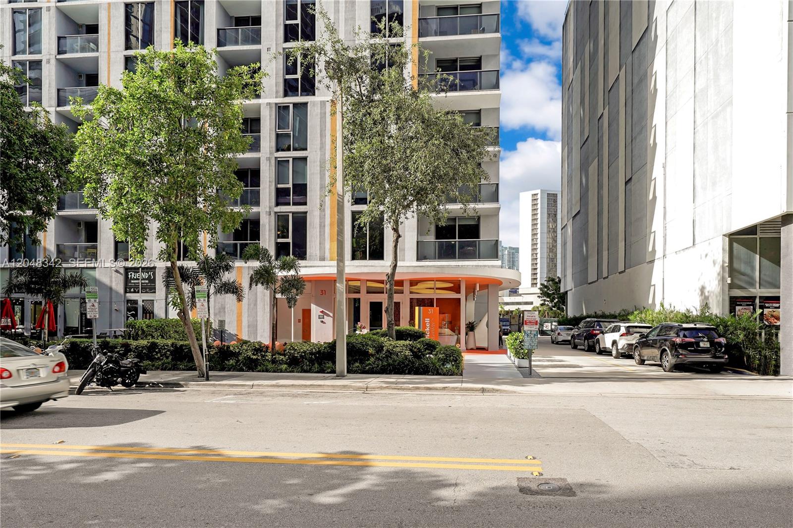 An exterior view of a modern apartment building with an orange entrance and parked cars — 31 SE 6th St # 2706, Miami FL 33131, MIAMI, FL