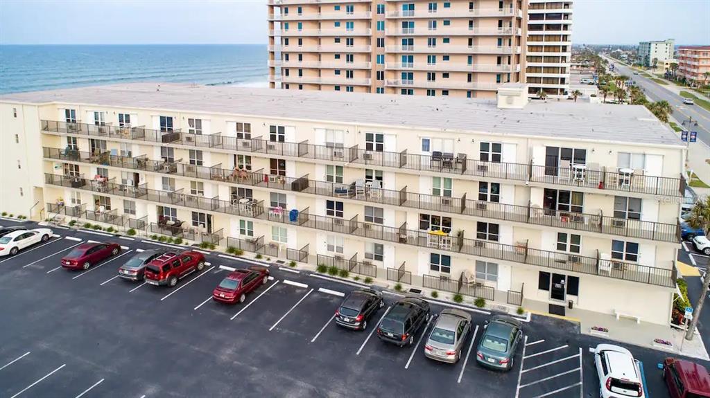 An aerial view shows a multi-story apartment building with balconies facing a parking lot and ocean — 3727 S ATLANTIC AVE UNIT 1120, DAYTONA BEACH, FL