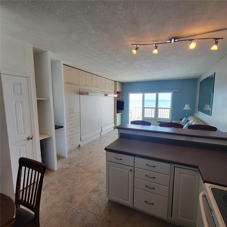 A kitchen with light cabinets and a breakfast bar overlooks a living area with ocean views — 3727 S ATLANTIC AVE UNIT 1120, DAYTONA BEACH, FL
