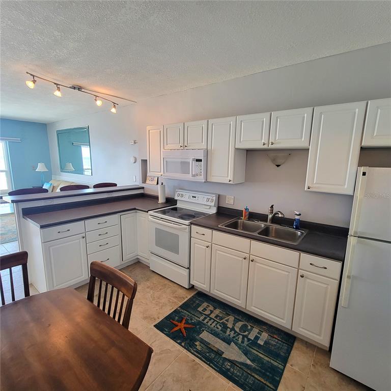 A kitchen with white cabinets, dark countertops, and a tile floor, opening to a living area — 3727 S ATLANTIC AVE UNIT 1120, DAYTONA BEACH, FL