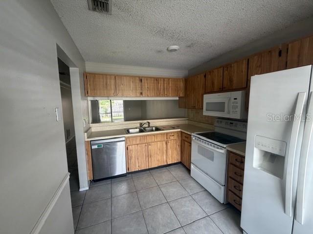 A kitchen features wood cabinets, a stainless steel dishwasher, a white stove, and tile flooring — 300 KENT PLACE, SAFETY HARBOR, FL