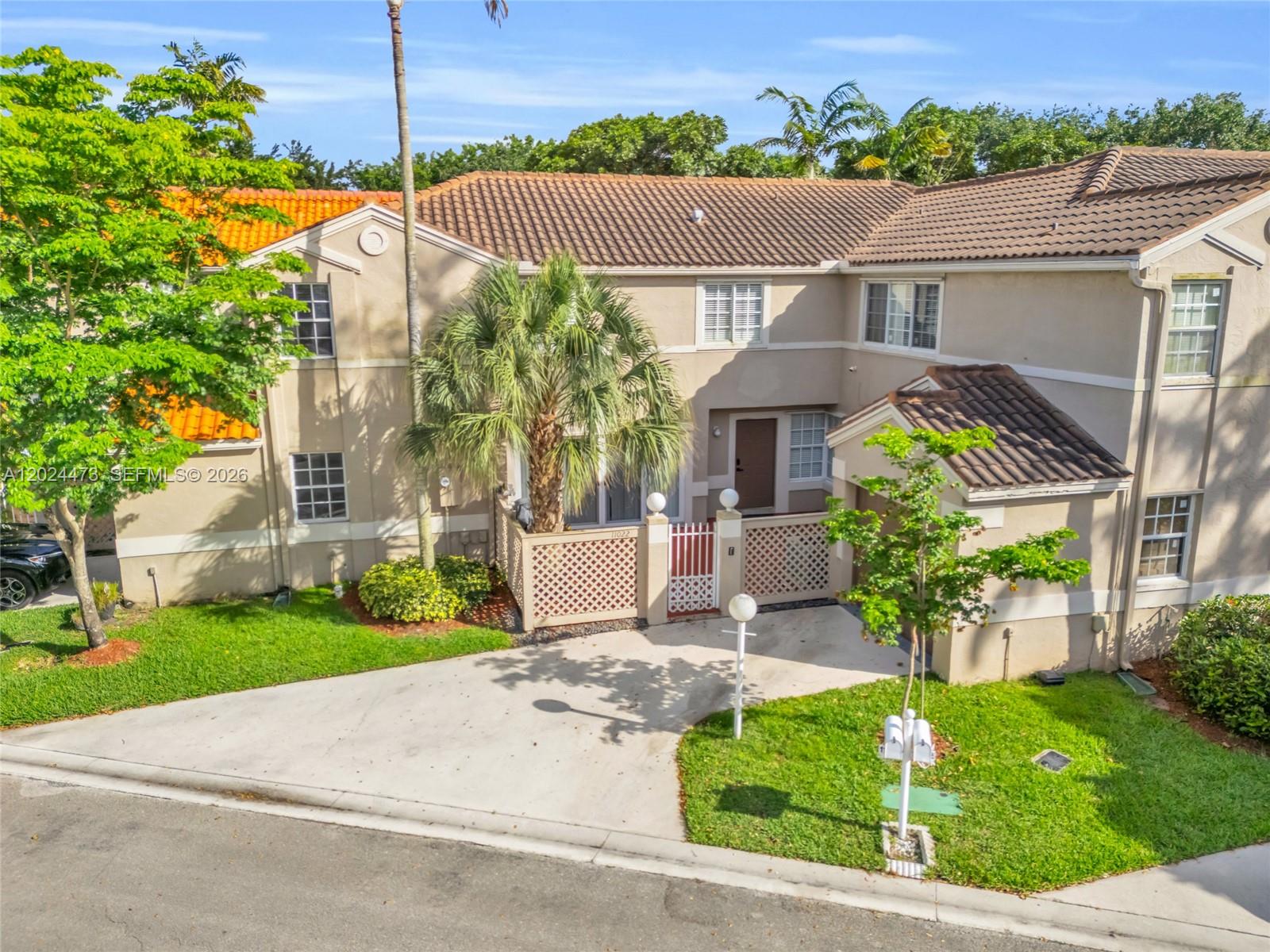 An exterior view of a two-story townhouse with a concrete driveway and a palm tree — 11022 Chandler Dr, Cooper City FL 33026, COOPER CITY, FL