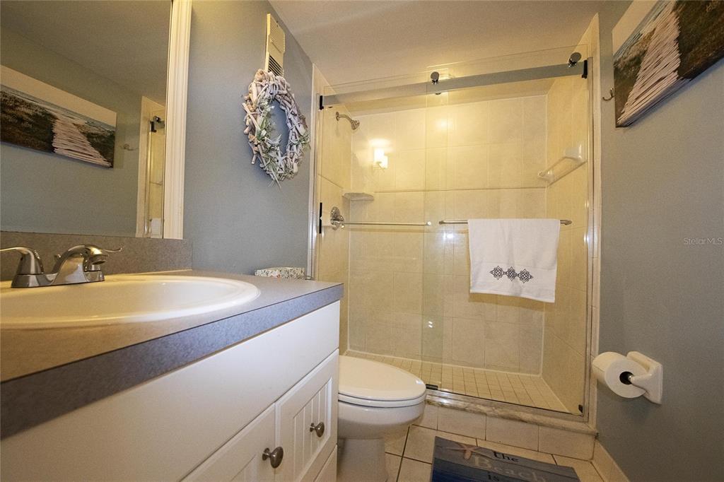 A bathroom features a white vanity, a toilet, and a glass-enclosed tiled shower — 1571 S ATLANTIC AVENUE UNIT 106, NEW SMYRNA BEACH, FL