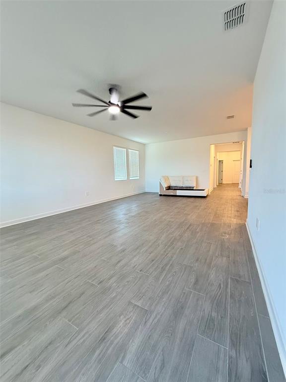 A spacious, empty living room features gray wood-look tile flooring and a ceiling fan — 2410 RELAXING LANE, KISSIMMEE, FL