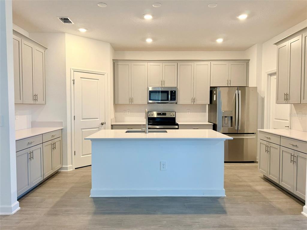 A kitchen features light gray cabinetry, stainless steel appliances, a white island, and wood-look flooring — 2410 RELAXING LANE, KISSIMMEE, FL