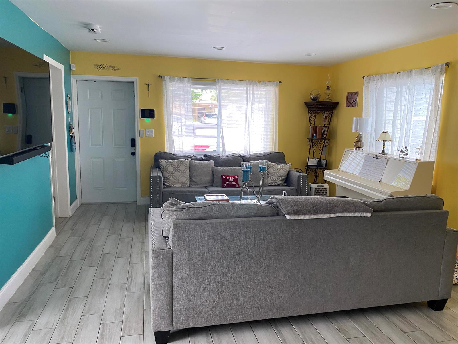 A living room features yellow walls, gray sofas, a white piano, and light wood-look flooring — 416 N D Street # 2, FL 33460, FL