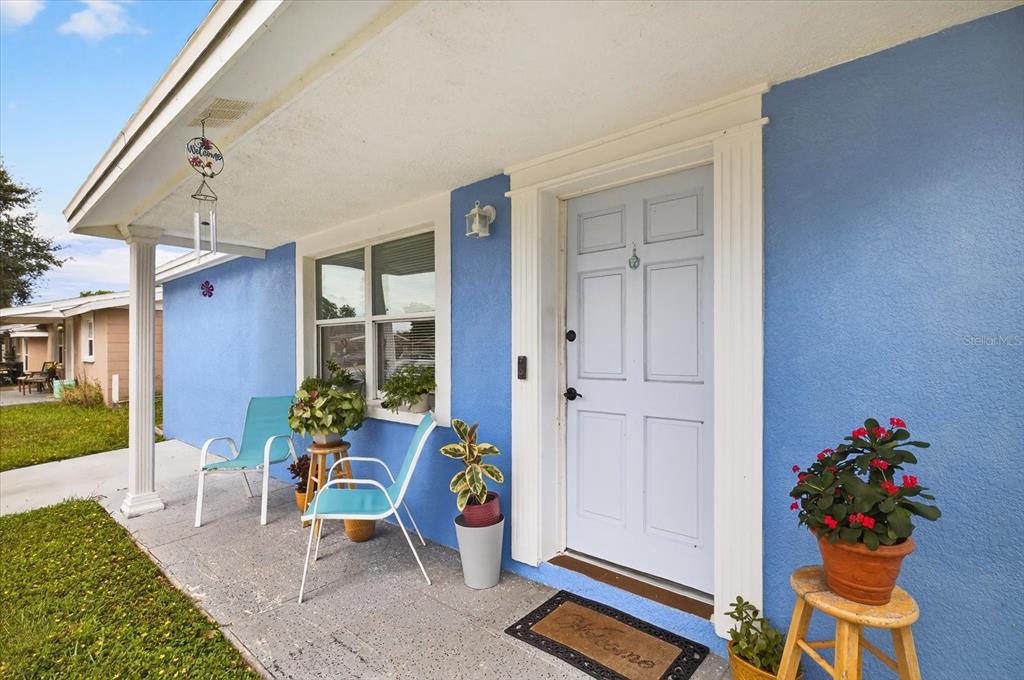 A blue house exterior features a front porch with chairs, potted plants, and a door — 7811 FOX HOLLOW DRIVE, PORT RICHEY, FL