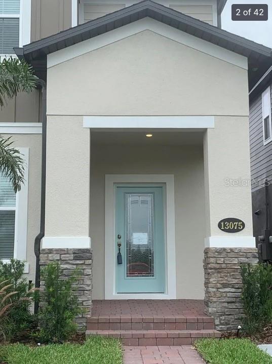 The front entrance features a light blue door, stone base pillars, and brick steps — 13075 SPRING GROVE WAY, WINTER GARDEN, FL