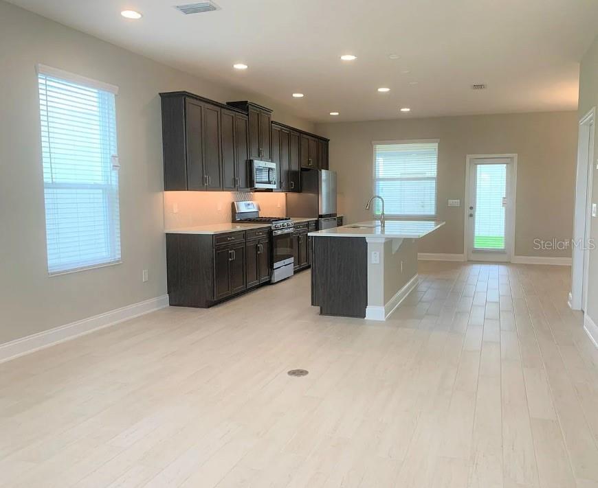 A modern kitchen features dark wood cabinets, a central island, and light-colored tile flooring — 13075 SPRING GROVE WAY, WINTER GARDEN, FL