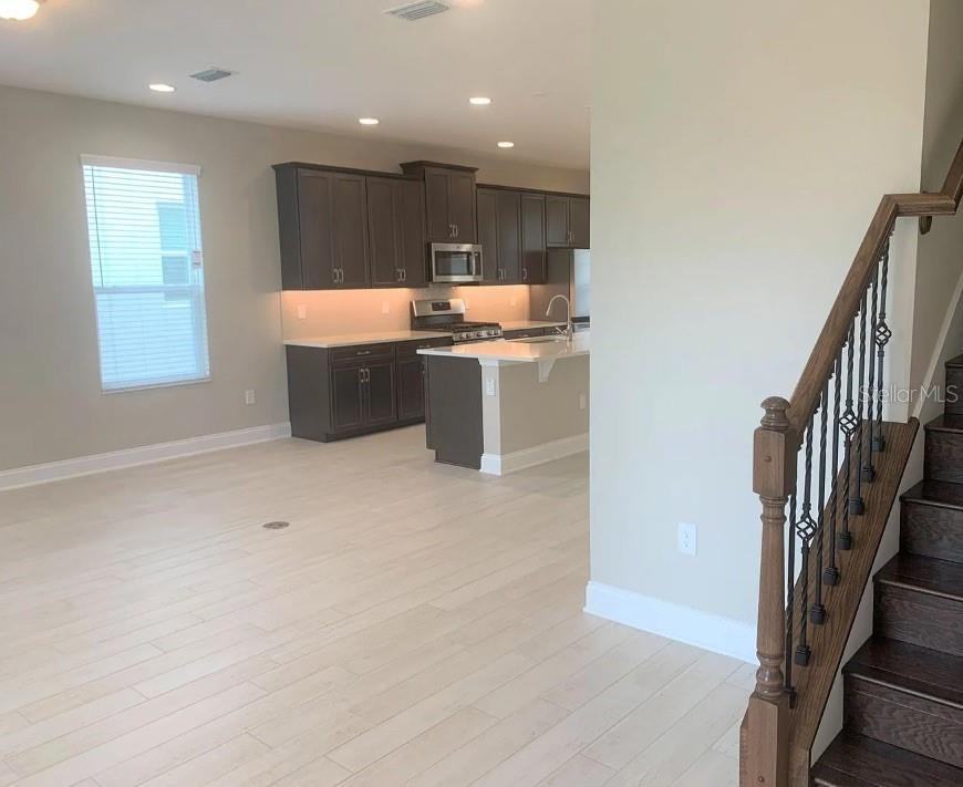 An open-concept kitchen with dark cabinets and a center island overlooks a living area — 13075 SPRING GROVE WAY, WINTER GARDEN, FL