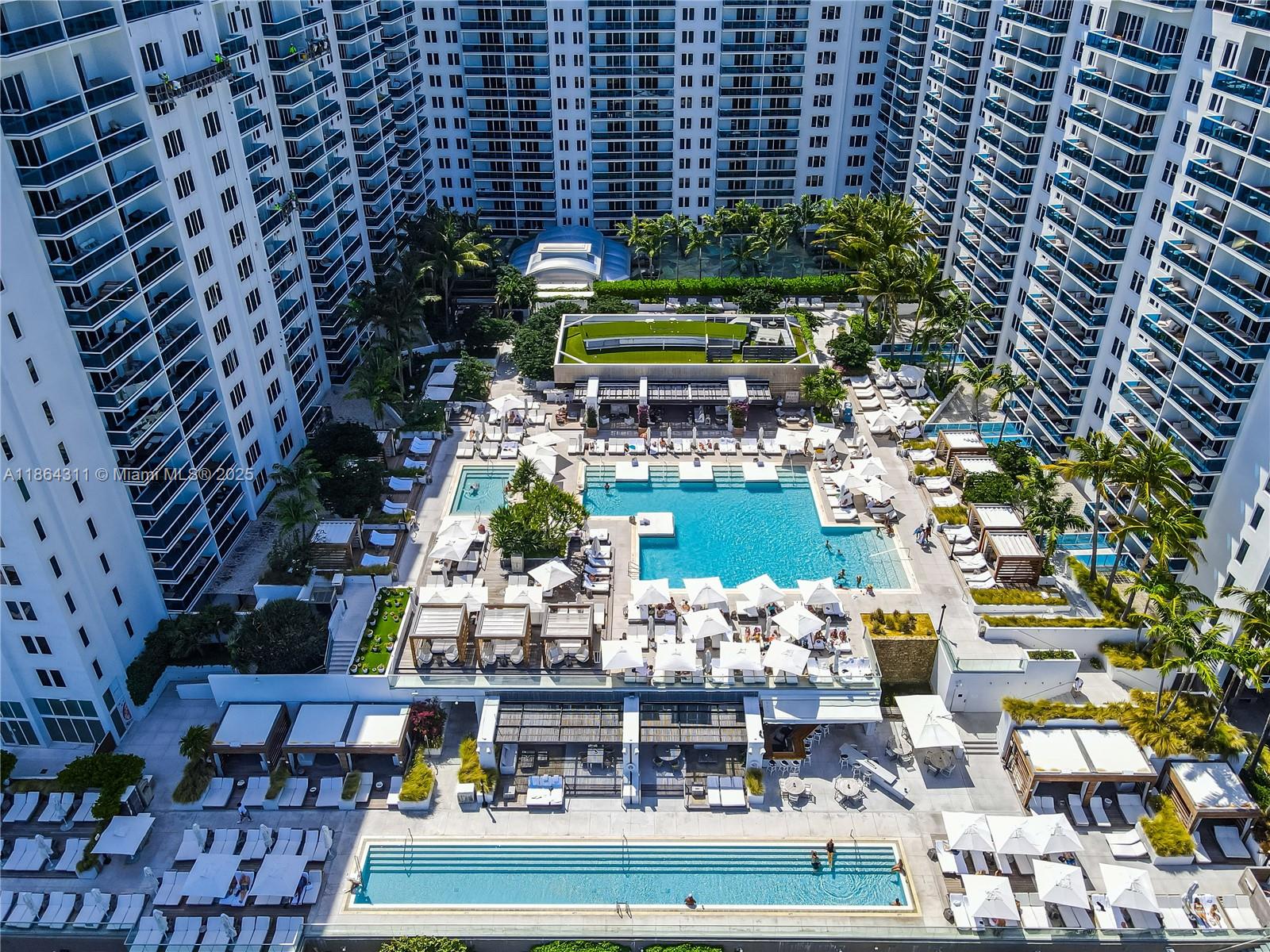 An aerial view shows a large apartment complex courtyard featuring multiple swimming pools and cabanas — 2301 Collins Ave # 542, Miami Beach FL 33139, MIAMI BEACH, FL