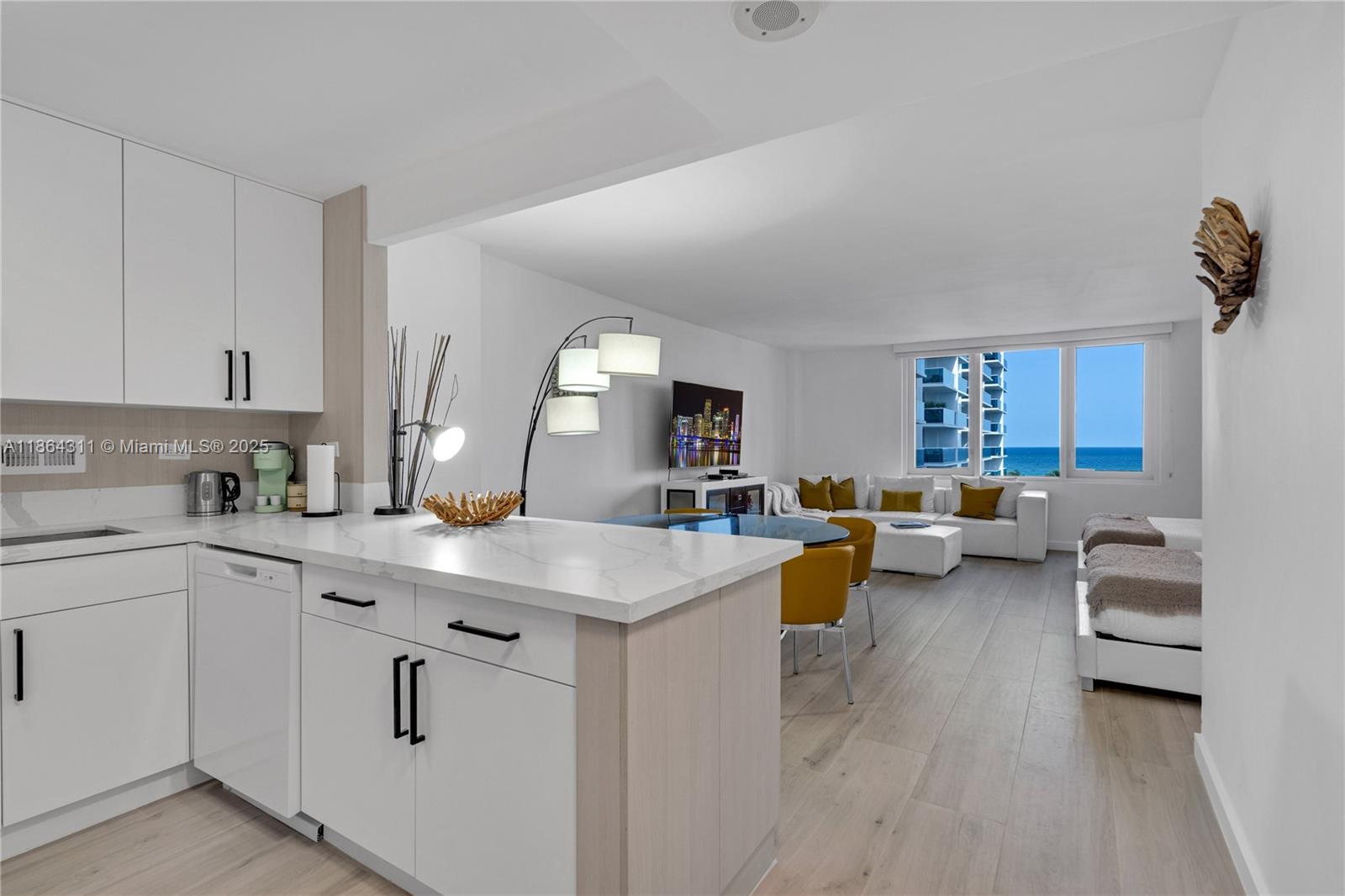 A modern kitchen with white cabinets and marble countertops opens into a living area with ocean views — 2301 Collins Ave # 542, Miami Beach FL 33139, MIAMI BEACH, FL