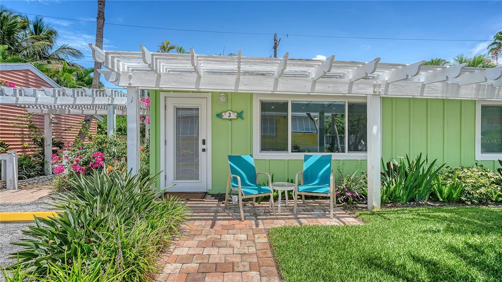 A light green cottage exterior features a white pergola, a brick walkway, and two chairs — 1603 GULF DRIVE N UNIT 3, BRADENTON BEACH, FL