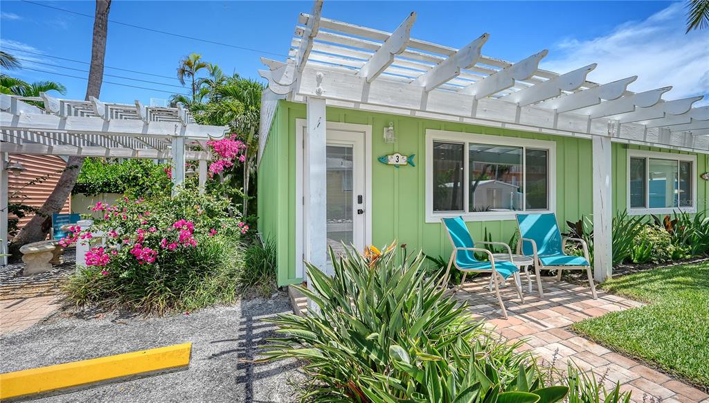 A light green cottage features a white pergola, two blue chairs, and tropical landscaping — 1603 GULF DRIVE N UNIT 3, BRADENTON BEACH, FL