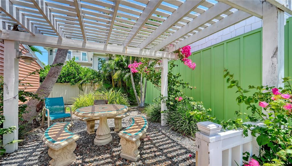 A white wooden pergola covers a stone patio with a table and curved benches — 1603 GULF DRIVE N UNIT 3, BRADENTON BEACH, FL