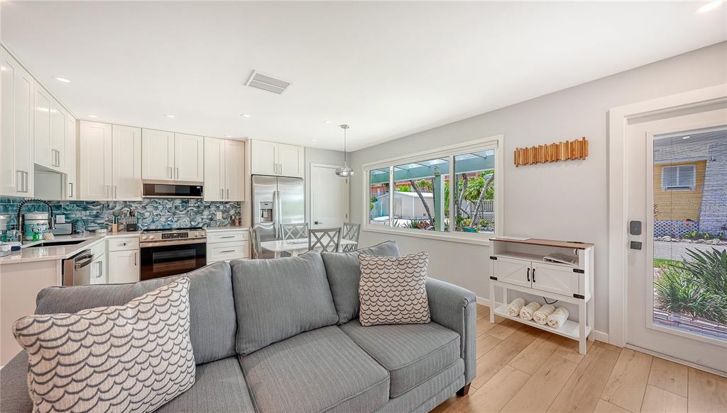 A living room with a grey sofa and a kitchen featuring white cabinets and blue tile — 1603 GULF DRIVE N UNIT 3, BRADENTON BEACH, FL