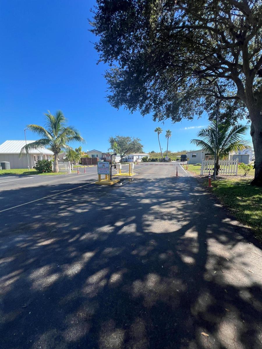 An asphalt driveway leads to a gated entrance of a residential community with palm trees — 7950 Florida 78, Okeechobee FL 34974, OKEECHOBEE, FL