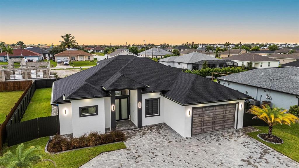 An aerial view of a modern single-story house with a dark roof and paved driveway — 1112 EMBERS PARKWAY W, CAPE CORAL, FL