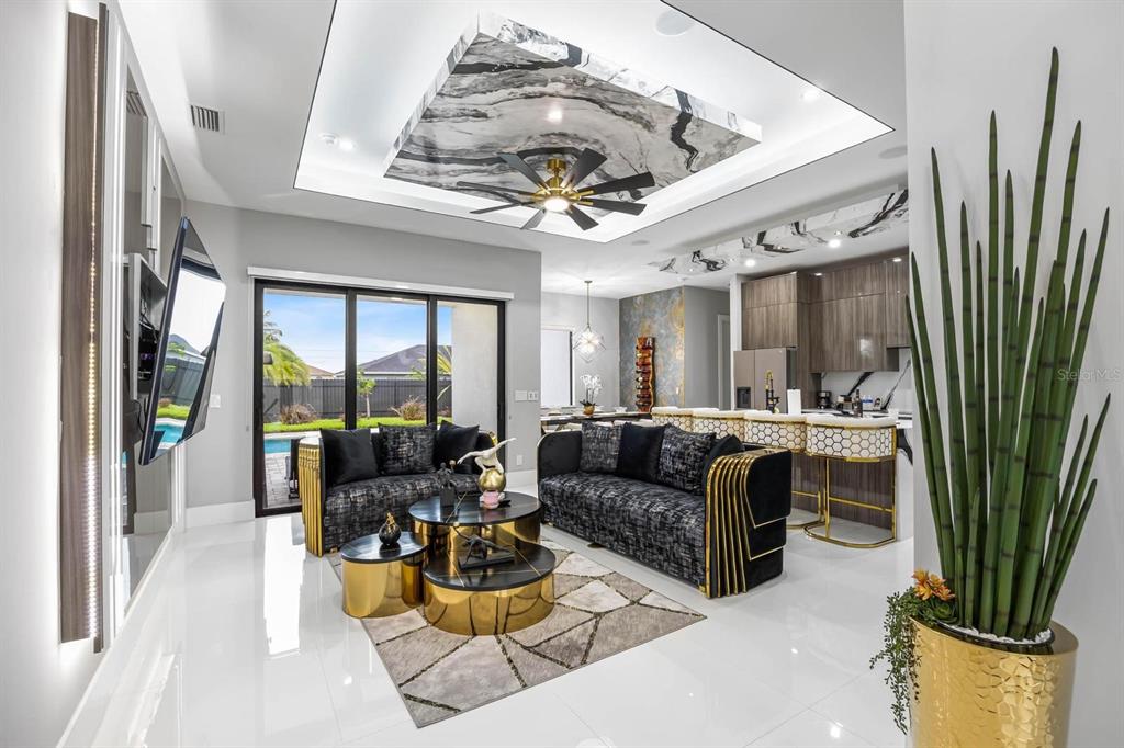 A modern living room features a marble ceiling accent, gold-accented furniture, and a kitchen island — 1112 EMBERS PARKWAY W, CAPE CORAL, FL