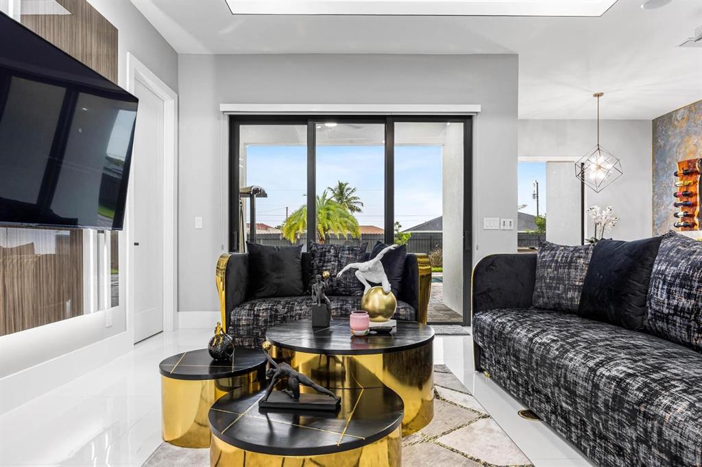 A modern living room features dark patterned sofas, gold-accented coffee tables, and large sliding doors — 1112 EMBERS PARKWAY W, CAPE CORAL, FL