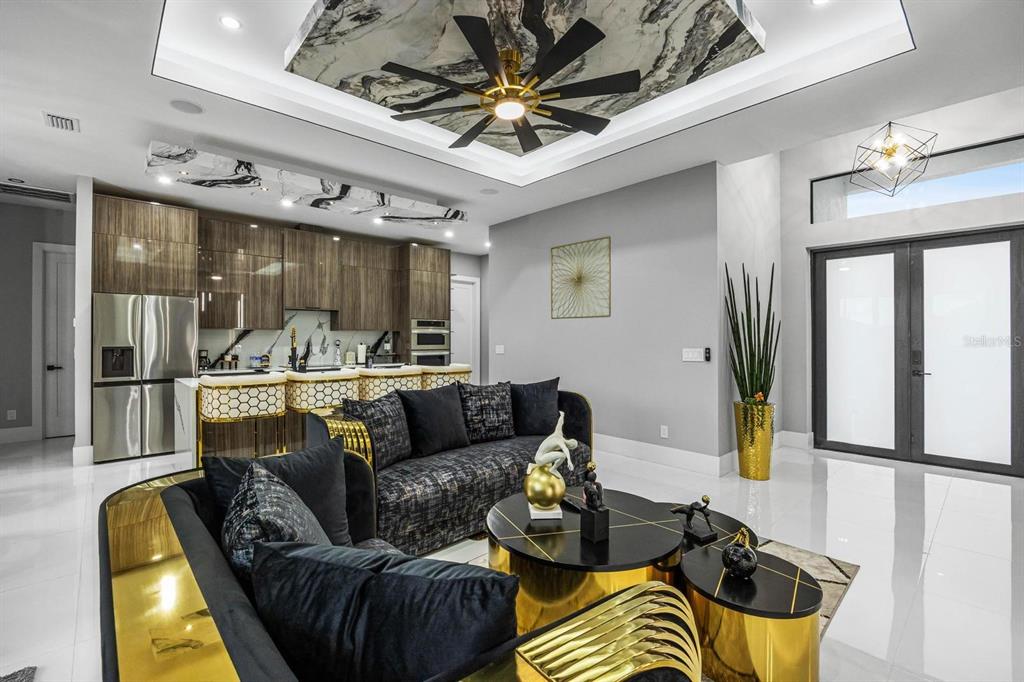 A modern living room features a marble ceiling accent, gold accents, and an open kitchen — 1112 EMBERS PARKWAY W, CAPE CORAL, FL