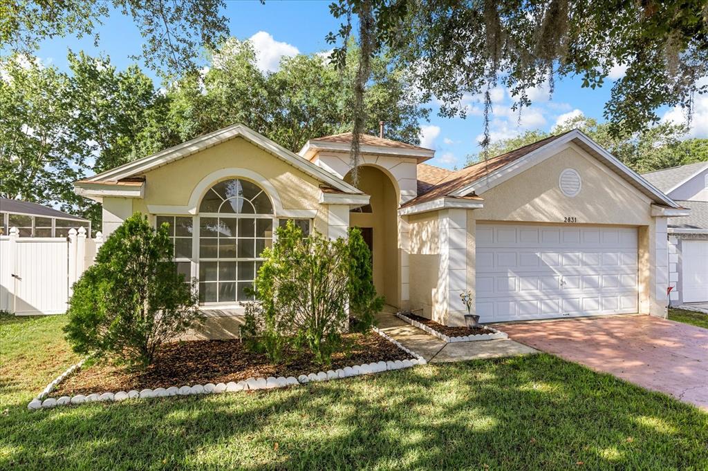 A single-story house with a beige stucco exterior, a two-car garage, and a front garden — 2831 WILSHIRE ROAD, CLERMONT, FL