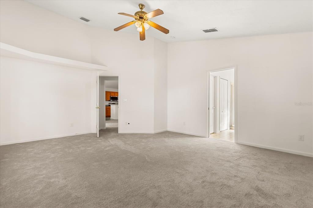 A spacious room with vaulted ceilings, gray carpeting, a ceiling fan, and two doorways — 2831 WILSHIRE ROAD, CLERMONT, FL