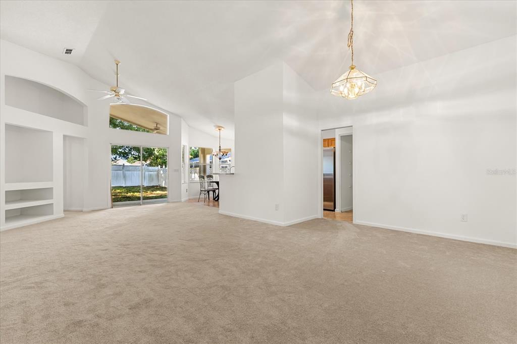 A spacious living room with beige carpeting, a vaulted ceiling, and a built-in wall unit — 2831 WILSHIRE ROAD, CLERMONT, FL