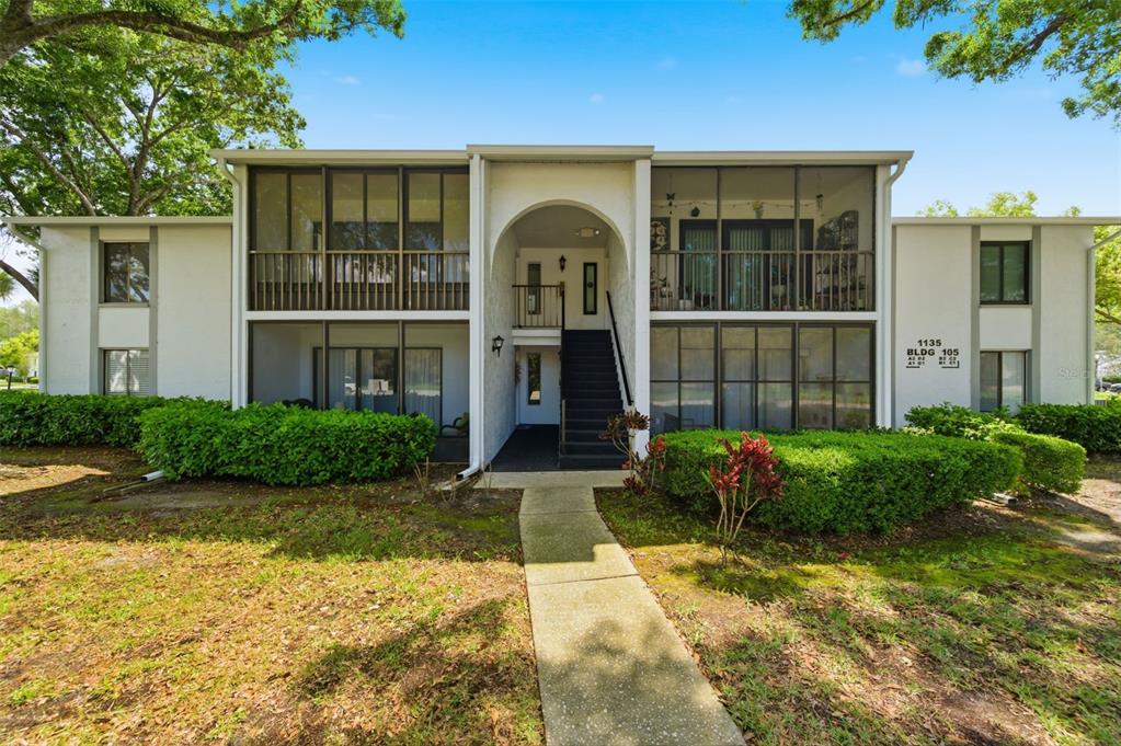 A two-story apartment building with screened balconies, a central staircase, and surrounding landscaping — 1135 PINE RIDGE CIRCLE W UNIT A2, TARPON SPRINGS, FL