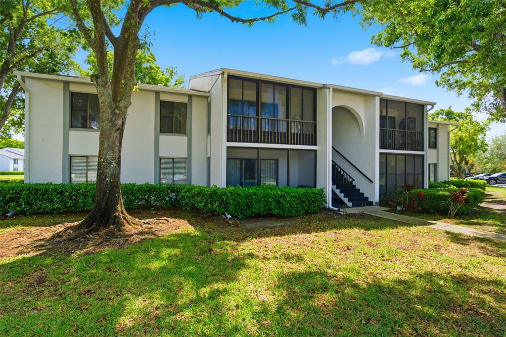 A two-story apartment building with screened balconies, a central staircase, and surrounding green landscaping — 1135 PINE RIDGE CIRCLE W UNIT A2, TARPON SPRINGS, FL