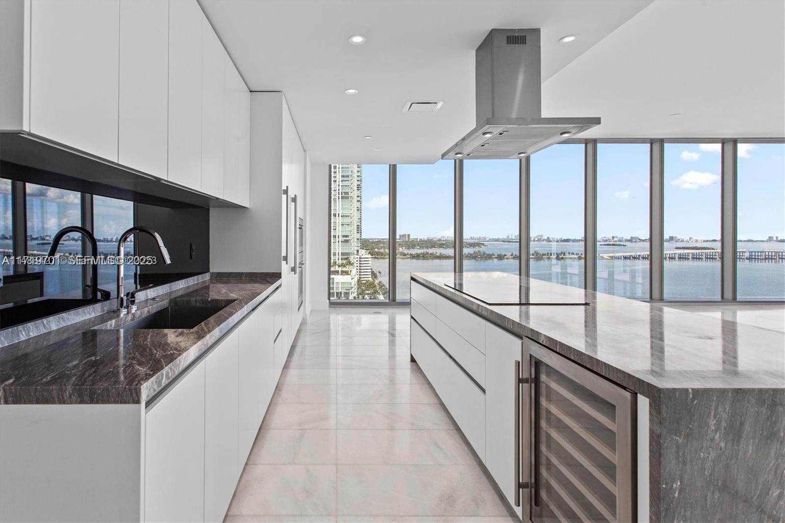 A modern kitchen features white cabinetry, marble countertops, a large island, and floor-to-ceiling windows — 700 NE 26th Ter # 2001, Miami FL 33137, MIAMI, FL