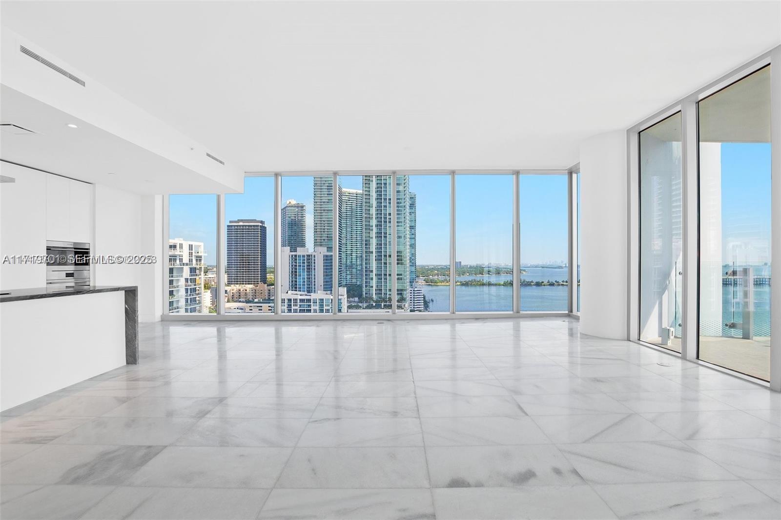 A bright, empty living room features white marble floors, floor-to-ceiling windows, and a modern kitchen — 700 NE 26th Ter # 2001, Miami FL 33137, MIAMI, FL