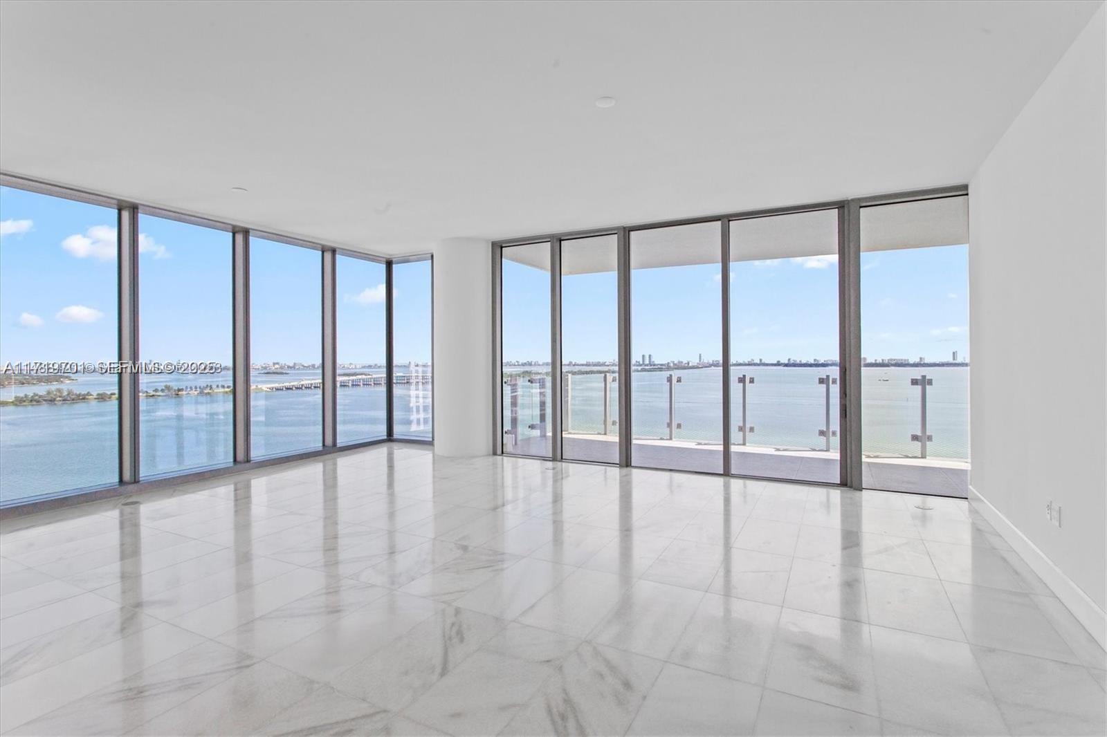 A bright, empty living room features floor-to-ceiling windows, marble flooring, and a balcony overlooking water — 700 NE 26th Ter # 2001, Miami FL 33137, MIAMI, FL