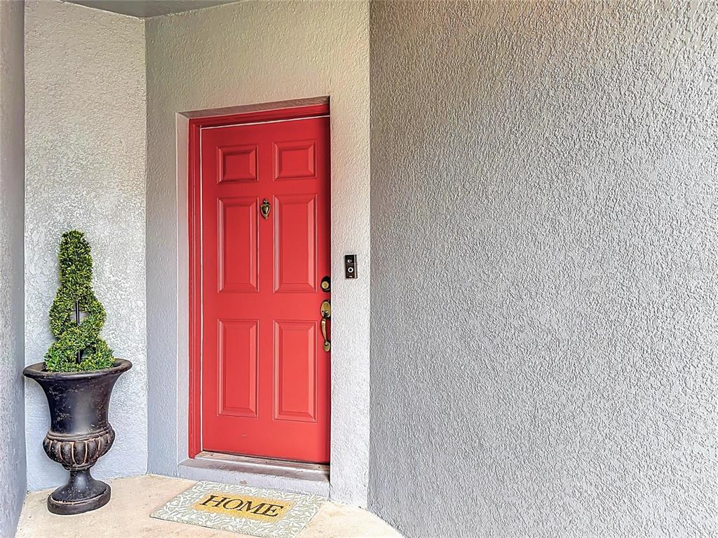 A red front door with a door knocker sits next to a potted topiary plant — 9379 FLOWERING COTTONWOOD ROAD UNIT 28, ORLANDO, FL
