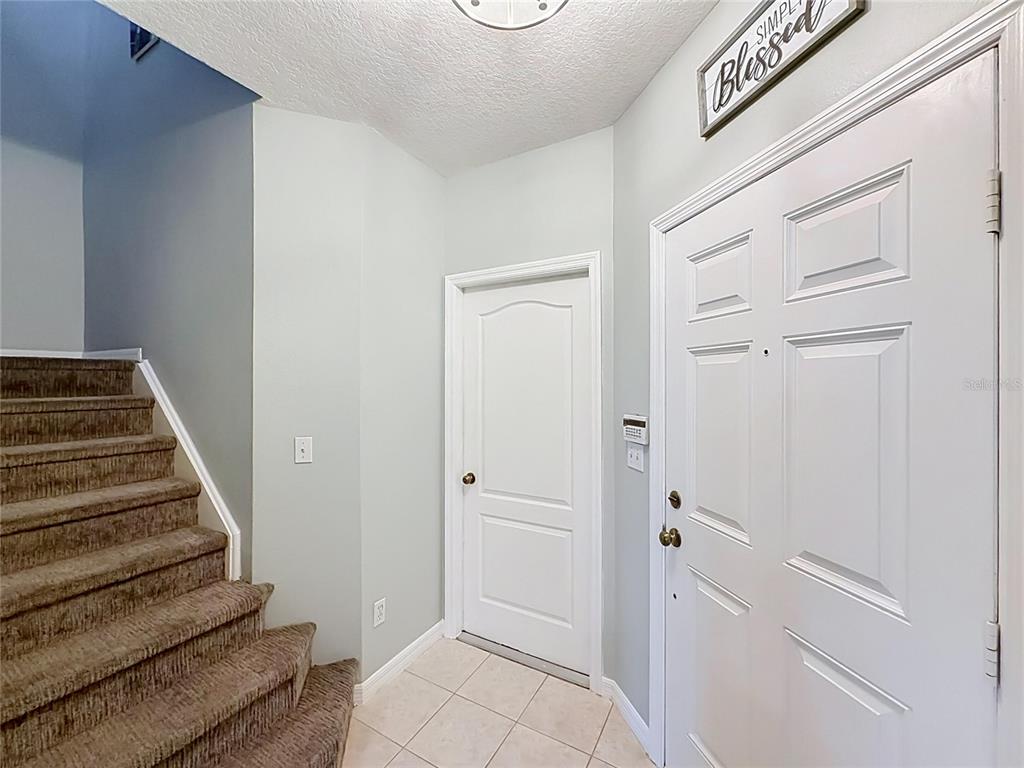An entryway features a carpeted staircase, a white front door, and a small interior door — 9379 FLOWERING COTTONWOOD ROAD UNIT 28, ORLANDO, FL