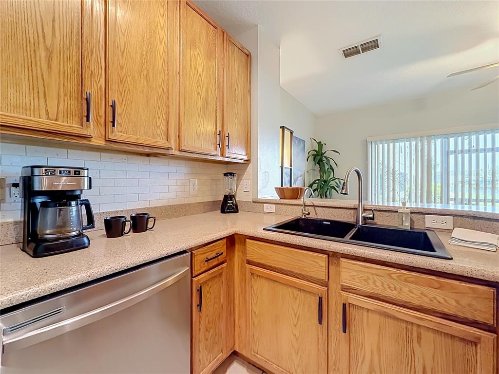 A kitchen features oak cabinets, a black double sink, and a stainless steel dishwasher — 9379 FLOWERING COTTONWOOD ROAD UNIT 28, ORLANDO, FL