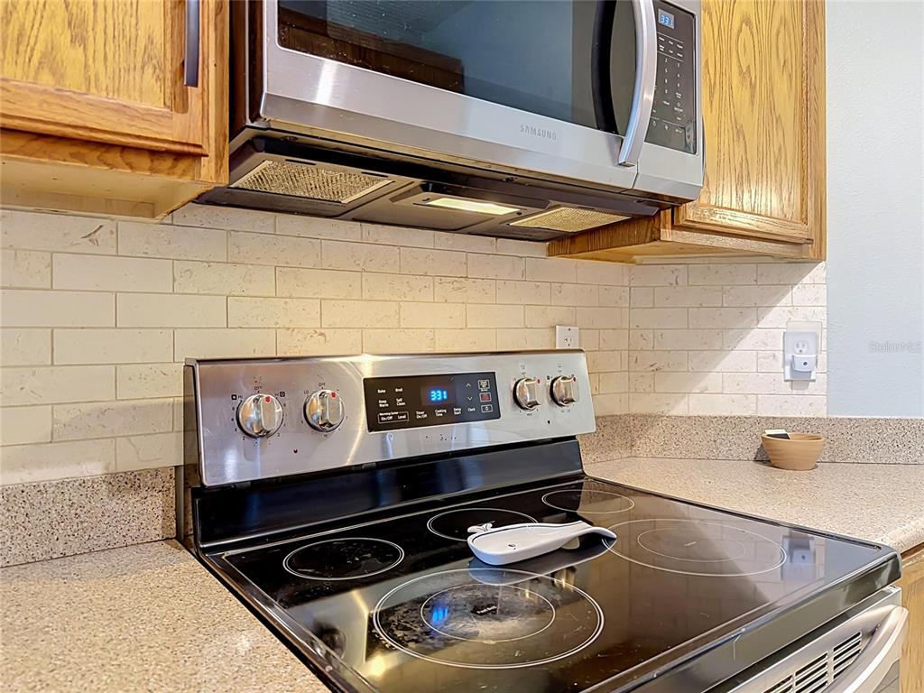 A stainless steel stove and microwave are installed in a kitchen with tiled backsplash — 9379 FLOWERING COTTONWOOD ROAD UNIT 28, ORLANDO, FL