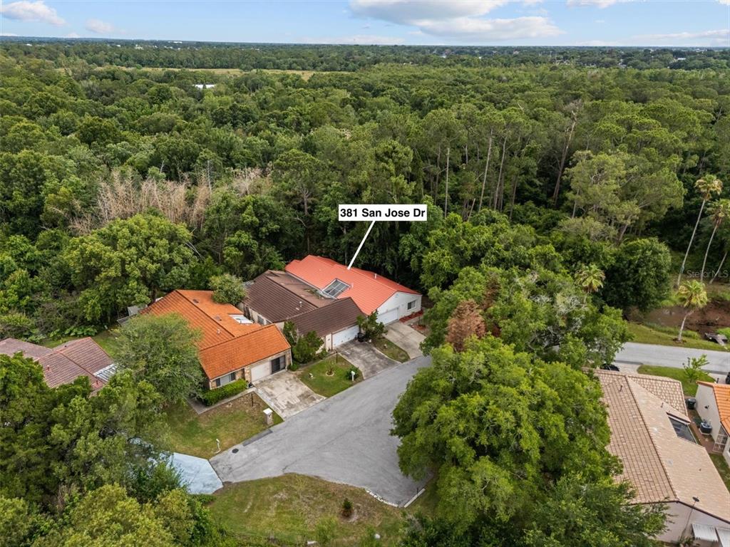 An aerial view shows two adjacent houses with orange tile roofs surrounded by dense trees — 381 SAN JOSE DRIVE, WINTER HAVEN, FL