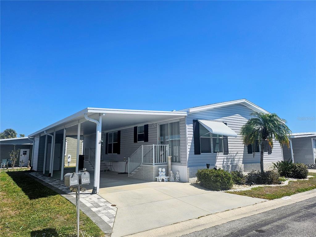 A light gray manufactured home features a covered carport, concrete driveway, and white railing — 3319 OVERCUP OAK TERRACE, SARASOTA, FL