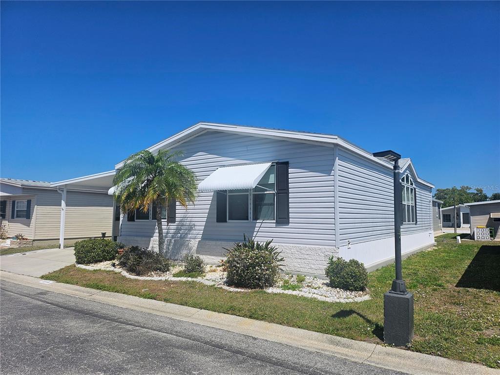 A light-colored manufactured home with a palm tree and a carport under a blue sky — 3319 OVERCUP OAK TERRACE, SARASOTA, FL