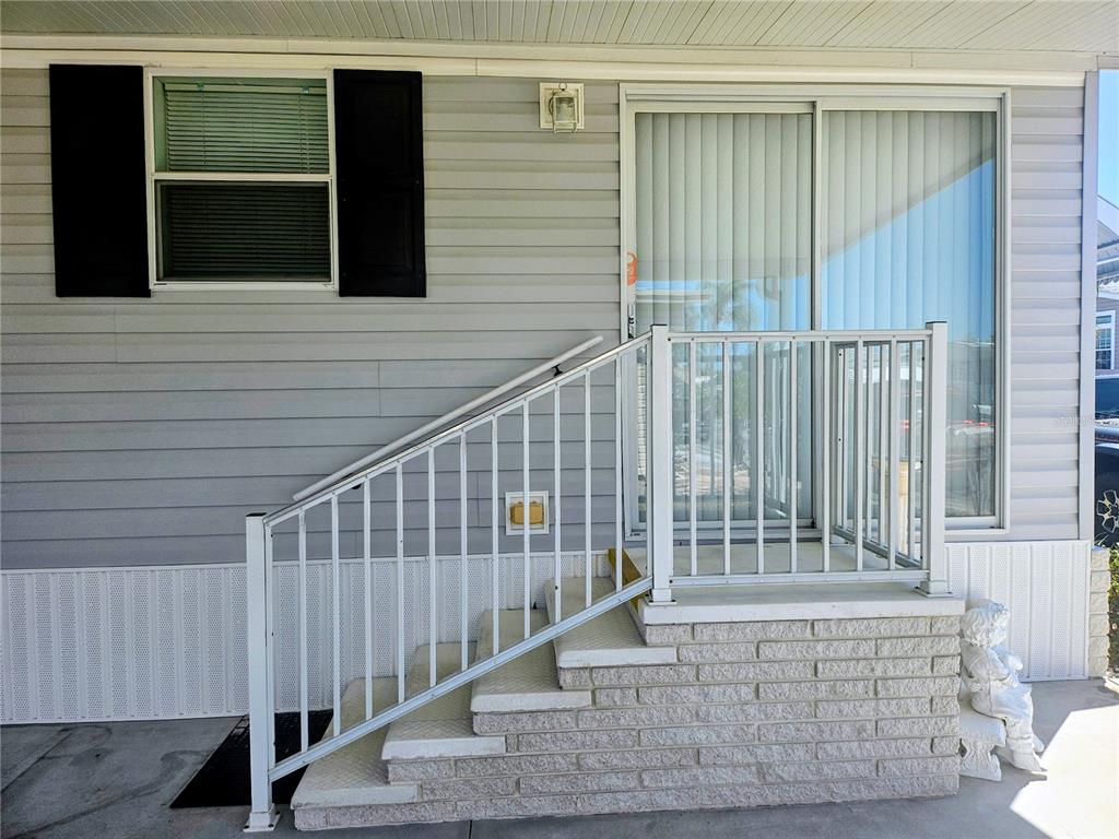 Exterior view of a mobile home entrance with concrete steps, metal railings, and sliding doors — 3319 OVERCUP OAK TERRACE, SARASOTA, FL