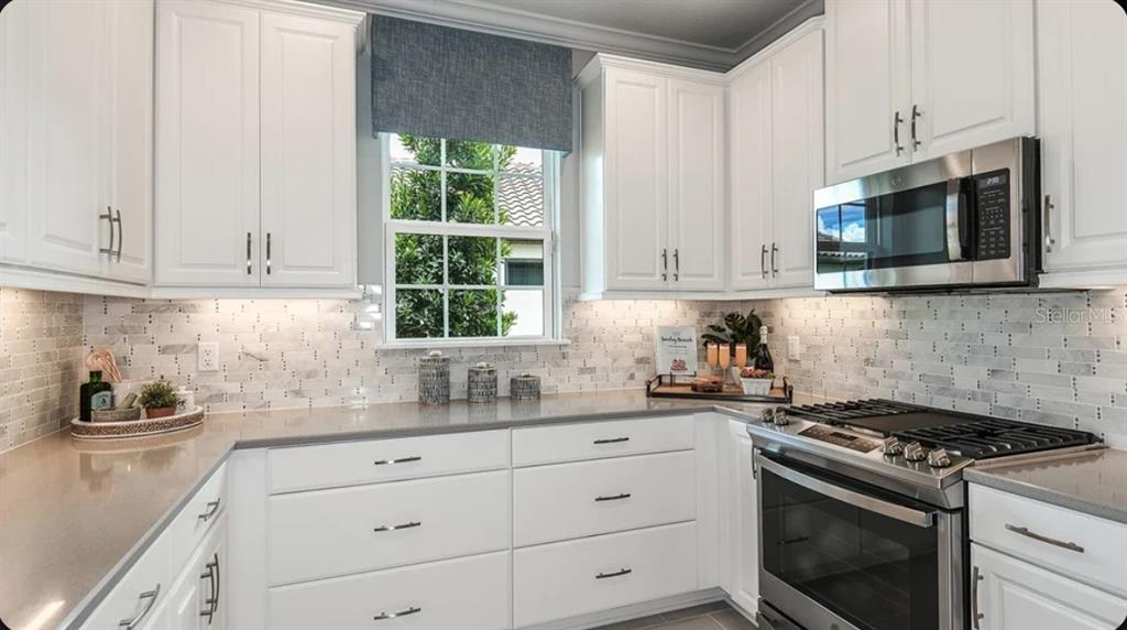 A kitchen features white cabinets, stainless steel appliances, a tiled backsplash, and a window — 13328 SANTINI CIRCLE, ENGLEWOOD, FL