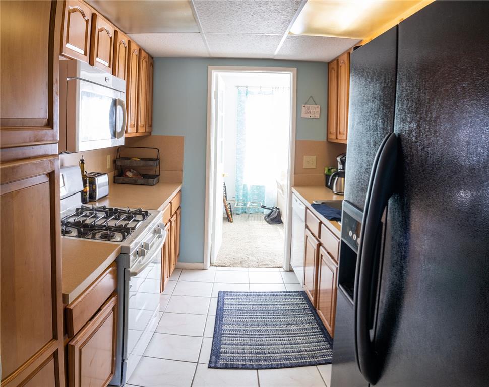 A galley kitchen features wood cabinets, white appliances, tile flooring, and a doorway to outside — 3018 59TH STREET S UNIT 309, GULFPORT, FL