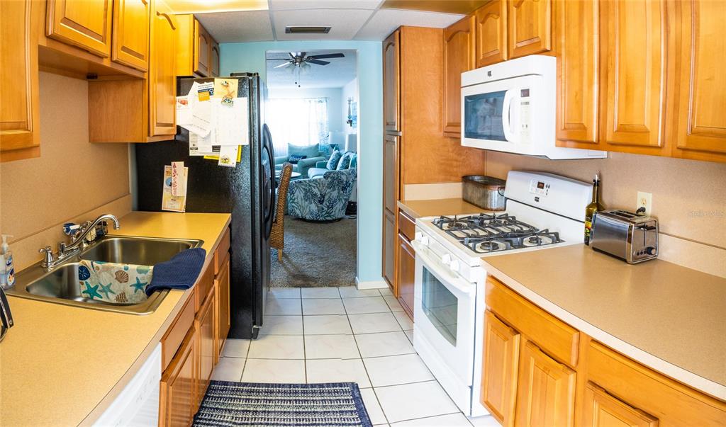 A galley kitchen features light wood cabinets, white appliances, and a tiled floor — 3018 59TH STREET S UNIT 309, GULFPORT, FL