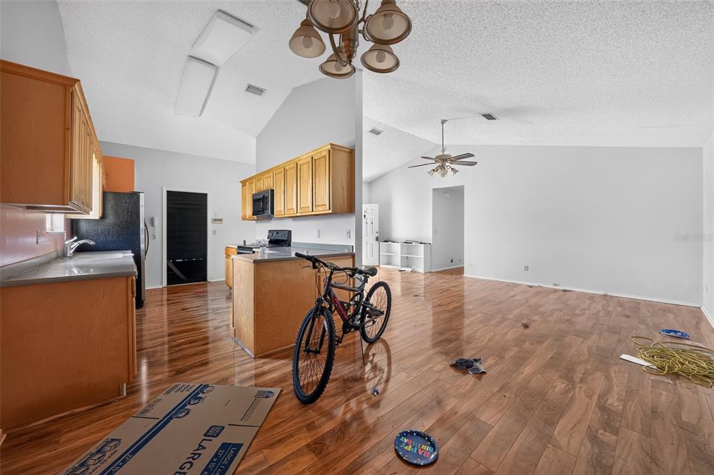 An open-concept living area features wood-look flooring, a vaulted ceiling with a fan, and a bicycle — 1632 CAINS AVENUE NW, PALM BAY, FL