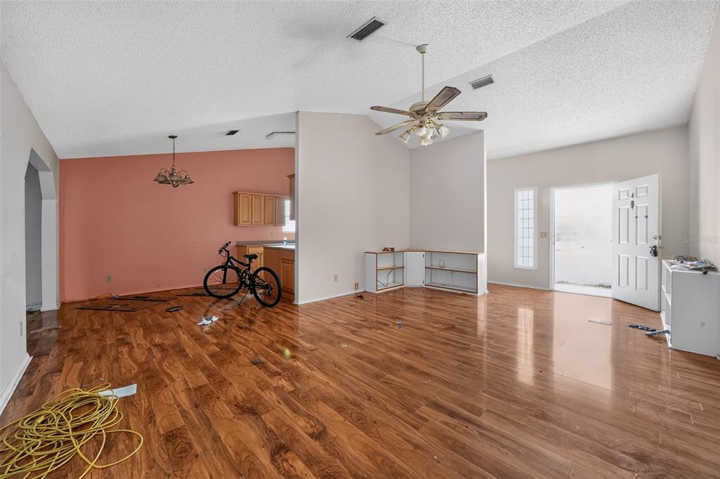 An open-concept kitchen and living area features wood-look flooring, light wood cabinets, and vaulted ceilings — 1632 CAINS AVENUE NW, PALM BAY, FL