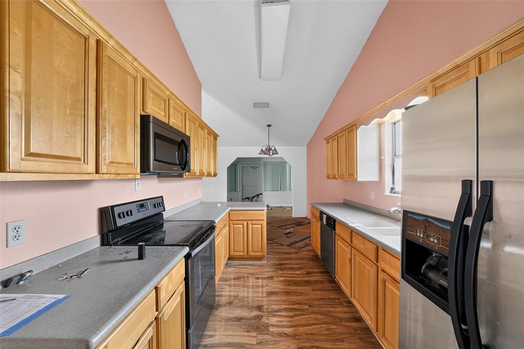 A galley kitchen features light wood cabinets, stainless steel appliances, and wood-look flooring — 1632 CAINS AVENUE NW, PALM BAY, FL