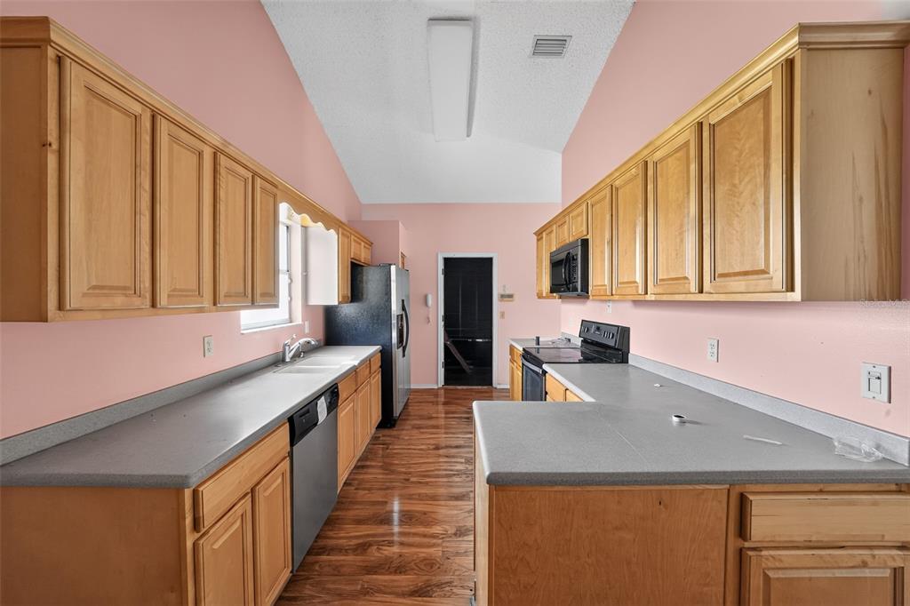 A kitchen with light wood cabinets, gray countertops, pink walls, and wood-look flooring — 1632 CAINS AVENUE NW, PALM BAY, FL