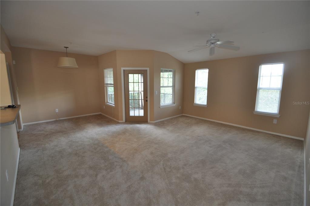An empty living room features beige carpet, tan walls, a ceiling fan, and a glass door — 408 SUMMIT RIDGE PLACE UNIT 316, LONGWOOD, FL